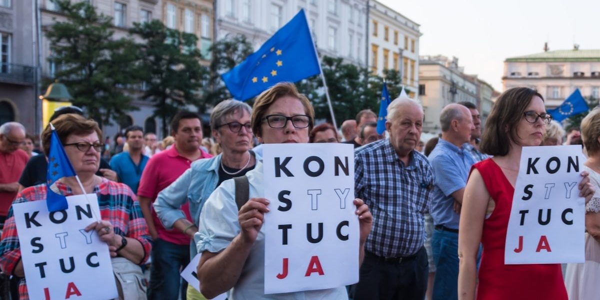 Many of the protesters are holding signs that read “KONSTYTUCJA,” which is the Polish word for “Constitution.” Some of the signs have certain letters highlighted, which is a common symbol used in Polish protests advocating for the defense of the constitution. Please attribute copyright © https://transly.eu/