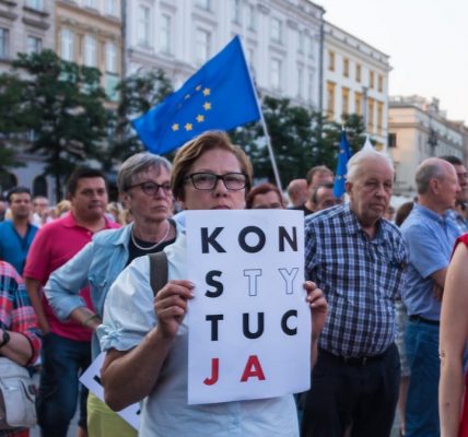Many of the protesters are holding signs that read “KONSTYTUCJA,” which is the Polish word for “Constitution.” Some of the signs have certain letters highlighted, which is a common symbol used in Polish protests advocating for the defense of the constitution. Please attribute copyright © https://transly.eu/