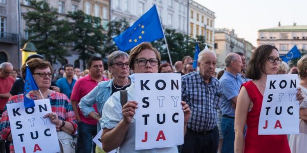 Many of the protesters are holding signs that read “KONSTYTUCJA,” which is the Polish word for “Constitution.” Some of the signs have certain letters highlighted, which is a common symbol used in Polish protests advocating for the defense of the constitution. Please attribute copyright © https://transly.eu/