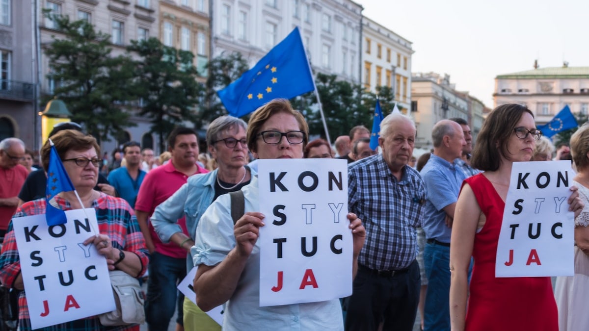 Many of the protesters are holding signs that read “KONSTYTUCJA,” which is the Polish word for “Constitution.” Some of the signs have certain letters highlighted, which is a common symbol used in Polish protests advocating for the defense of the constitution. Please attribute copyright © https://transly.eu/